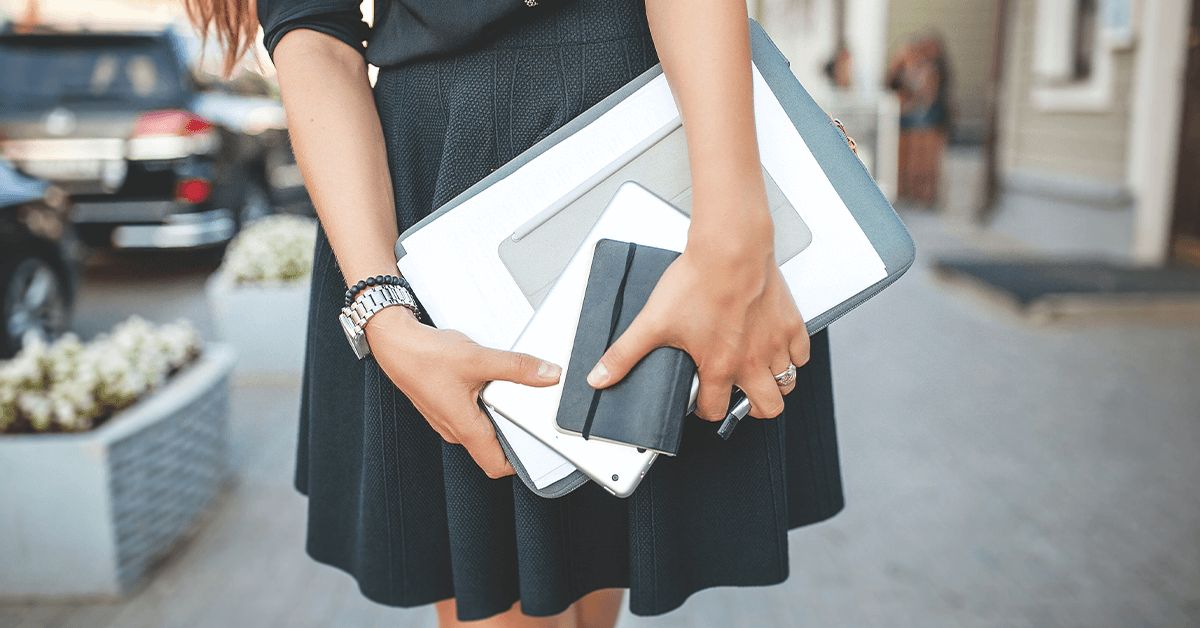 A woman in a black skirt holding a laptop and other personal items closely, symbolizing the need for discretion and control that is restored by urinary incontinence treatments.
